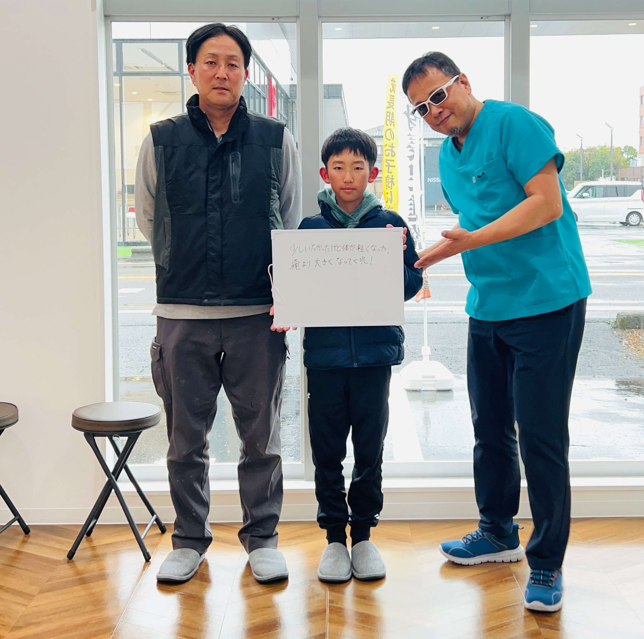 身長促進整体に感謝のメッセージを持つ小学生と父親・院長の写真
